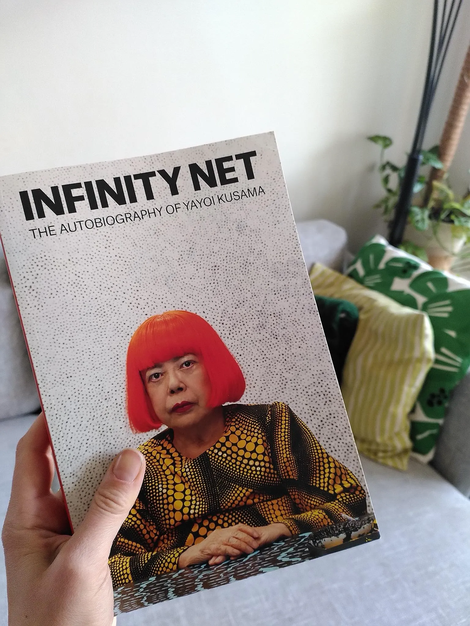 Js Hand hält das Buch „Infinity Net – The Autobiography of Yayoi Kusama“ ins Bild