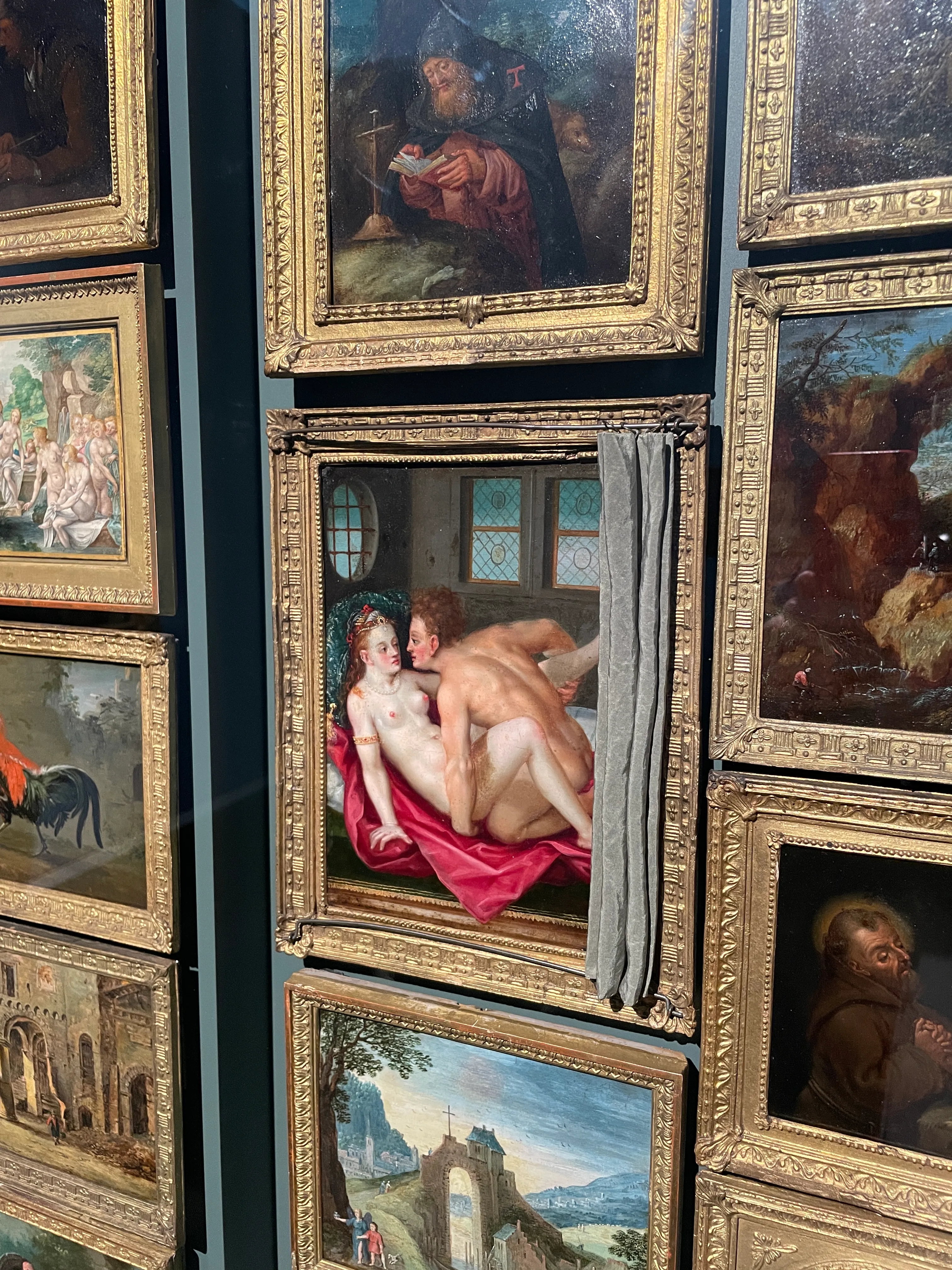 Eng gehangene Miniaturgemälde mit goldenem Rahmen. Ein freizügiger Liebesakt kann mit einem kleinen grauen Vorhang verdeckt werden.