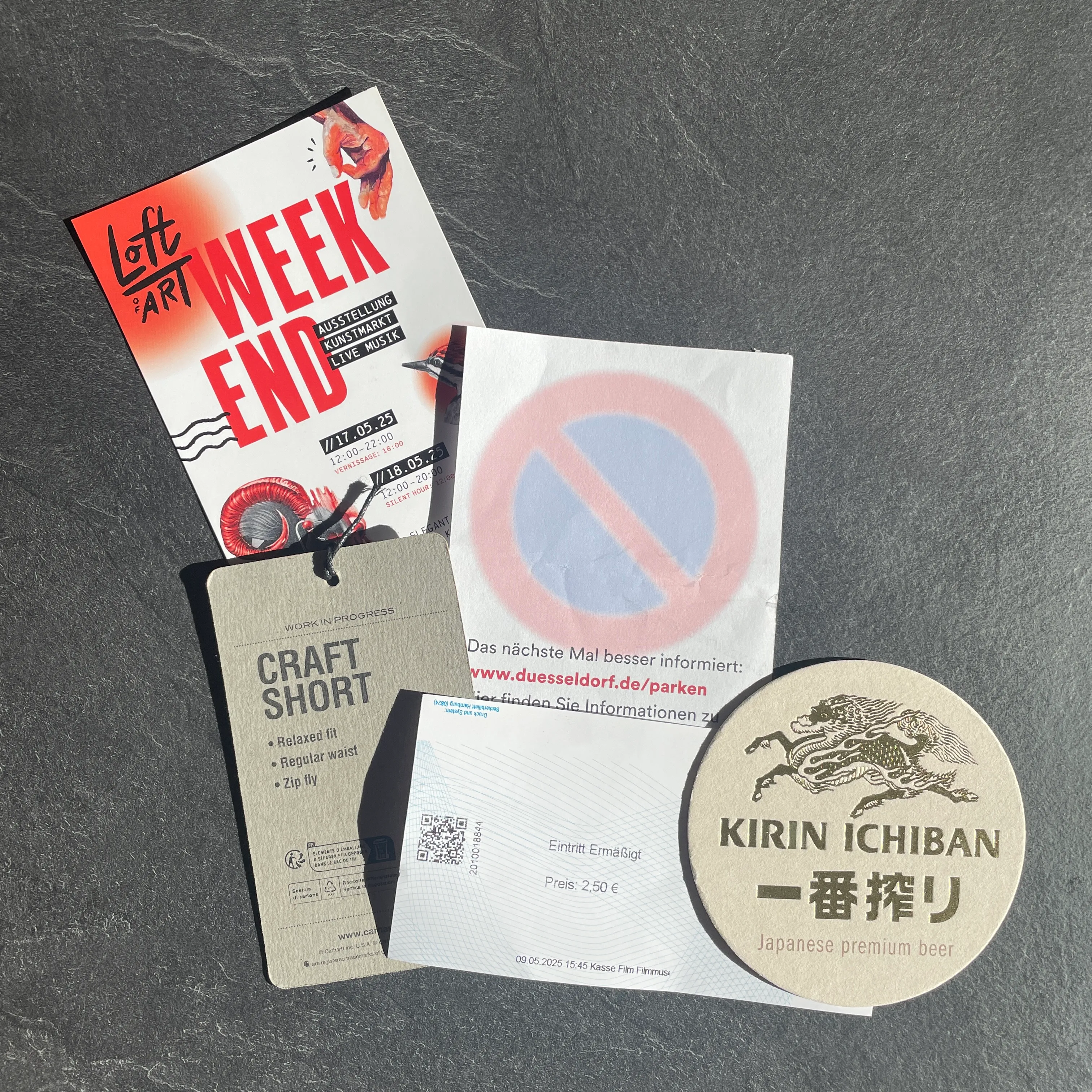 Die Zettelwirtschaft nach einem Tag in Düsseldorf: Flyer für einen Kunstmarkt, Hosen-Label vom Shoppen, Eintrittskarte vom Filmmuseum, japanischer Bierdeckel und ein Knöllchen.