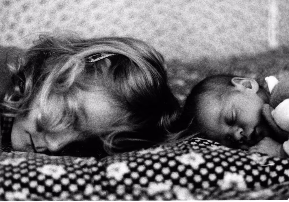 Zwei schlafende Menschen, Kopf an Kopf. Rechts ein kleines Baby, links vielleicht eine ältere Schwester oder die Mutter.