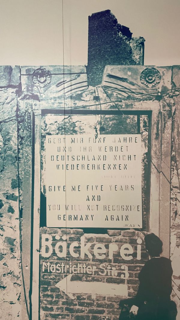 A signboard in bombed-out Cologne that says “Give me five years and you will not recognize Germany again,” an out-of-context quote by Adolf Hitler.