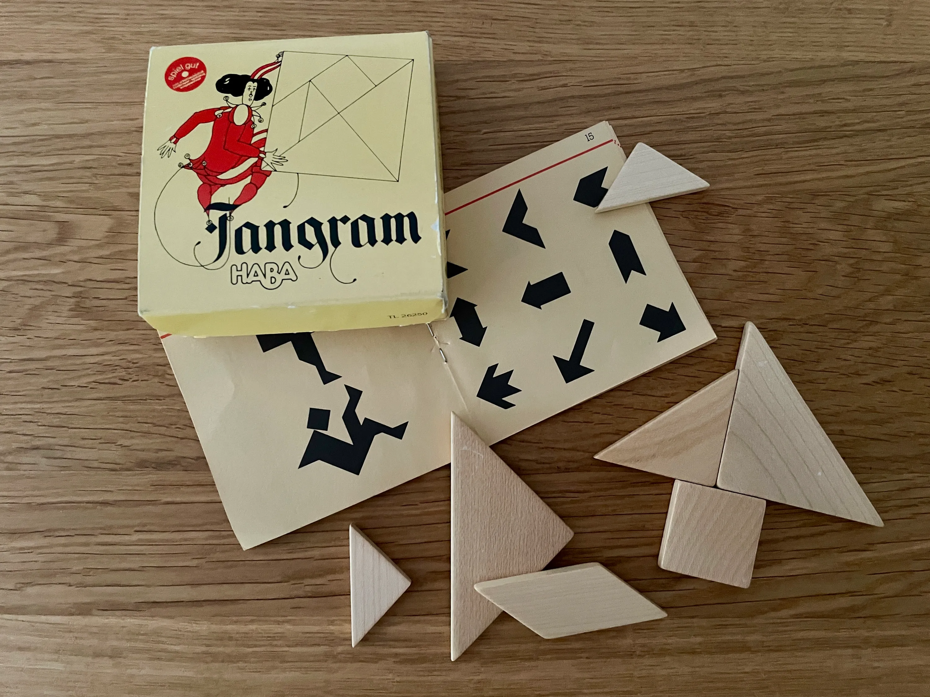 A wooden Tangram set with seven pieces, box, and instruction booklet laid out on my desk.